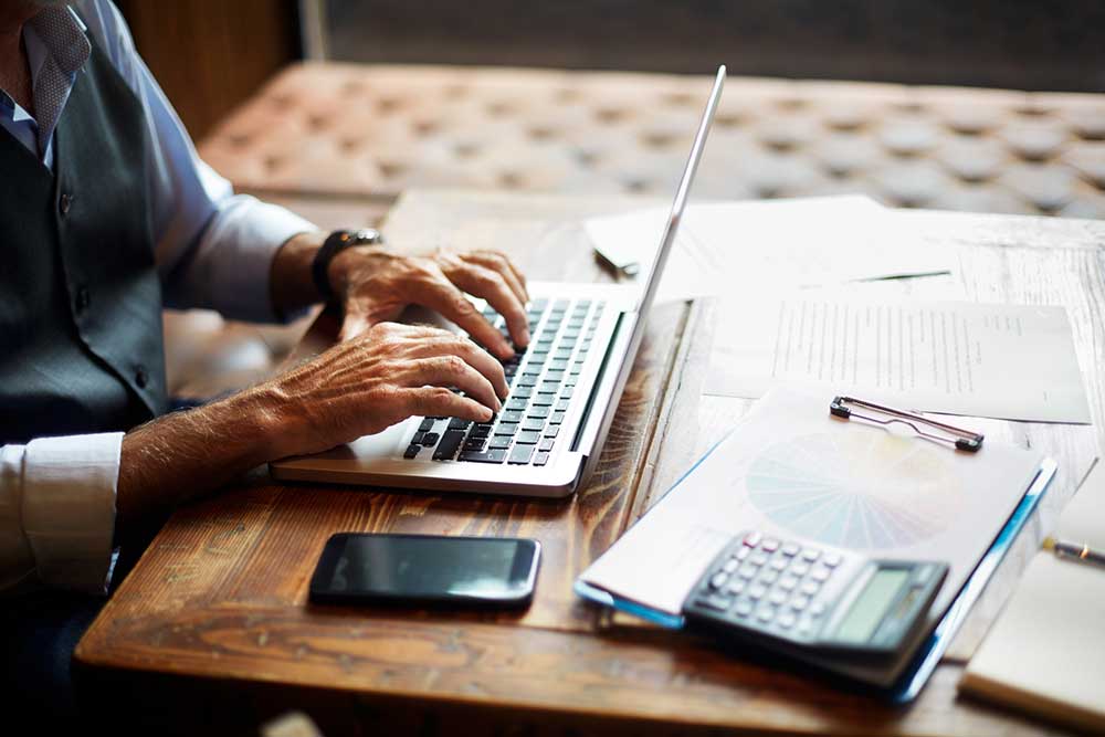 Person on a computer with calculator and accounting reports